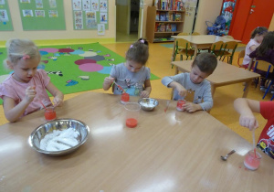 Czworo dzieci pipetkami wkraplają zabarwioną na pomarańczowo ciecz do słoiczków z roztworem soli.